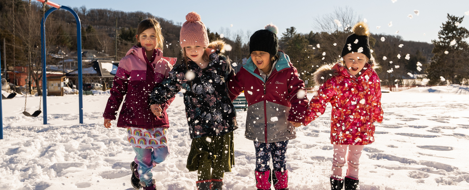 Four children playing in the snow with big smiles on their faces.